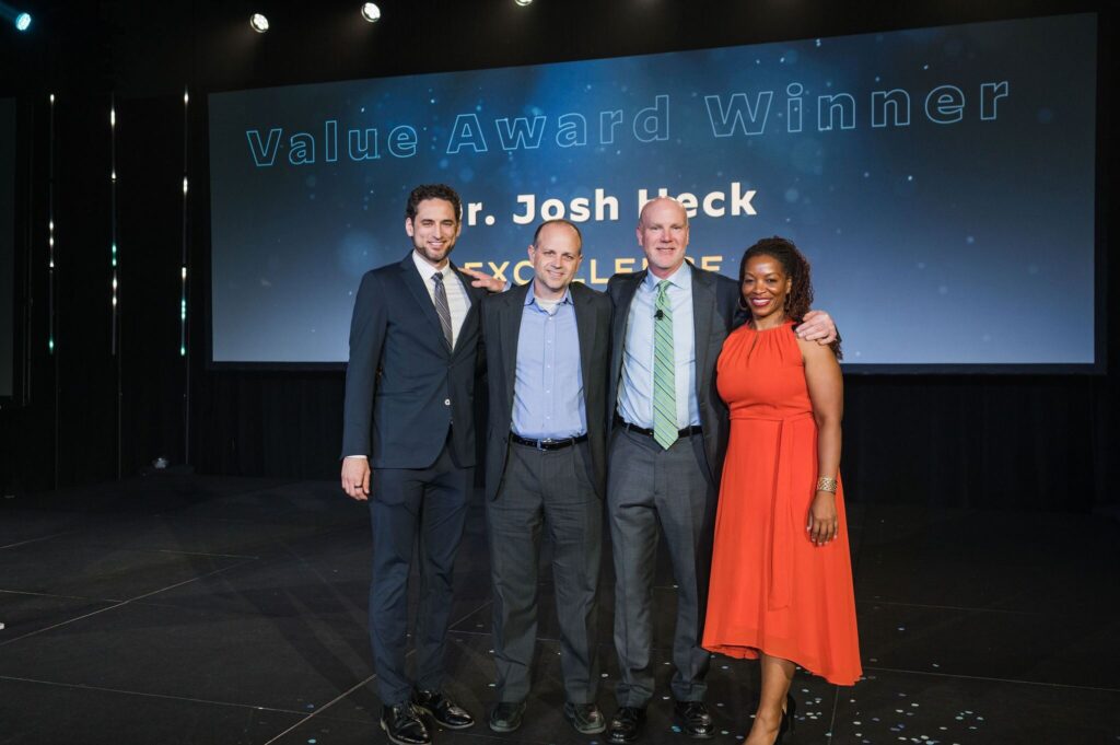 three men and one woman stand on stage smiling