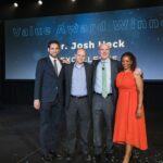 three men and one woman stand on stage smiling
