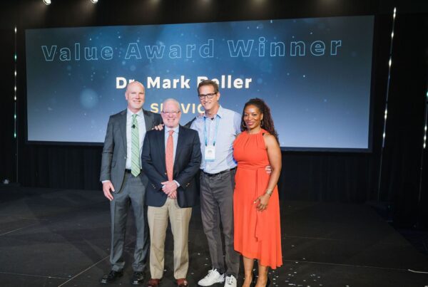 three men and one woman stand on stage smiling
