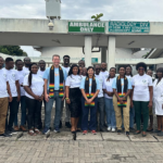 group of about 20 people, men and women, are posing and smiling together outside a hospital