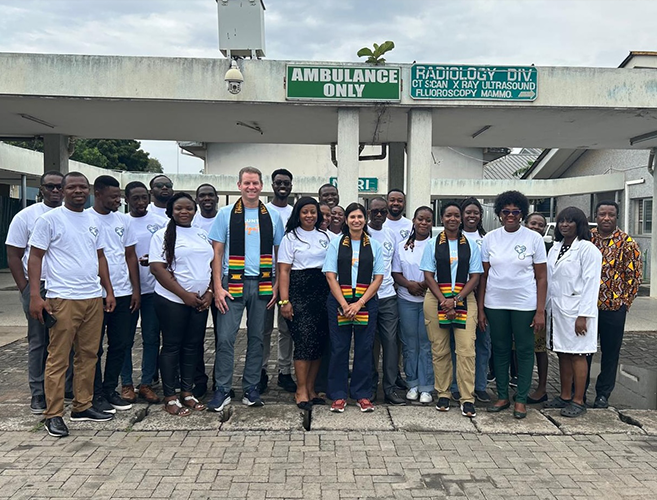 group of about 20 people, men and women, are posing and smiling together outside a hospital