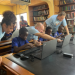 children being taught how to use computers in a classrooms by adult mentors